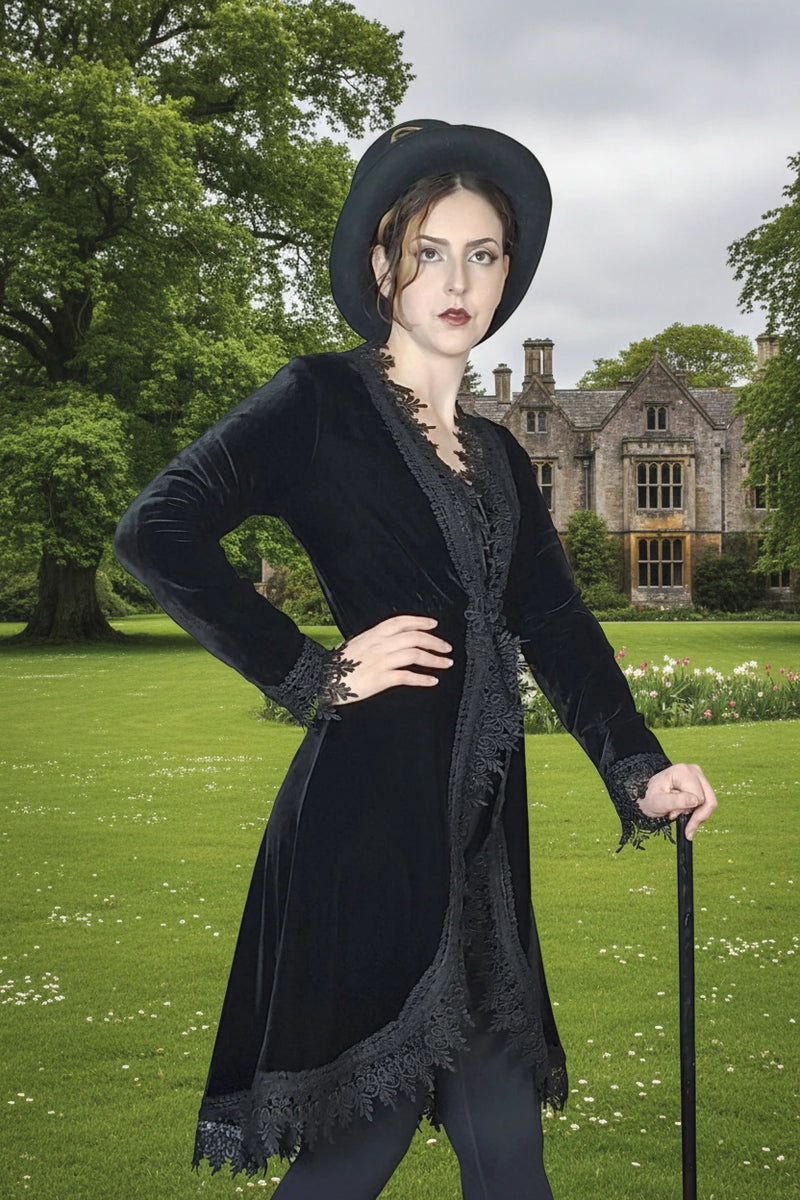 Woman in a black velvet coat with lace details and a hat, standing on a classic english green lawn