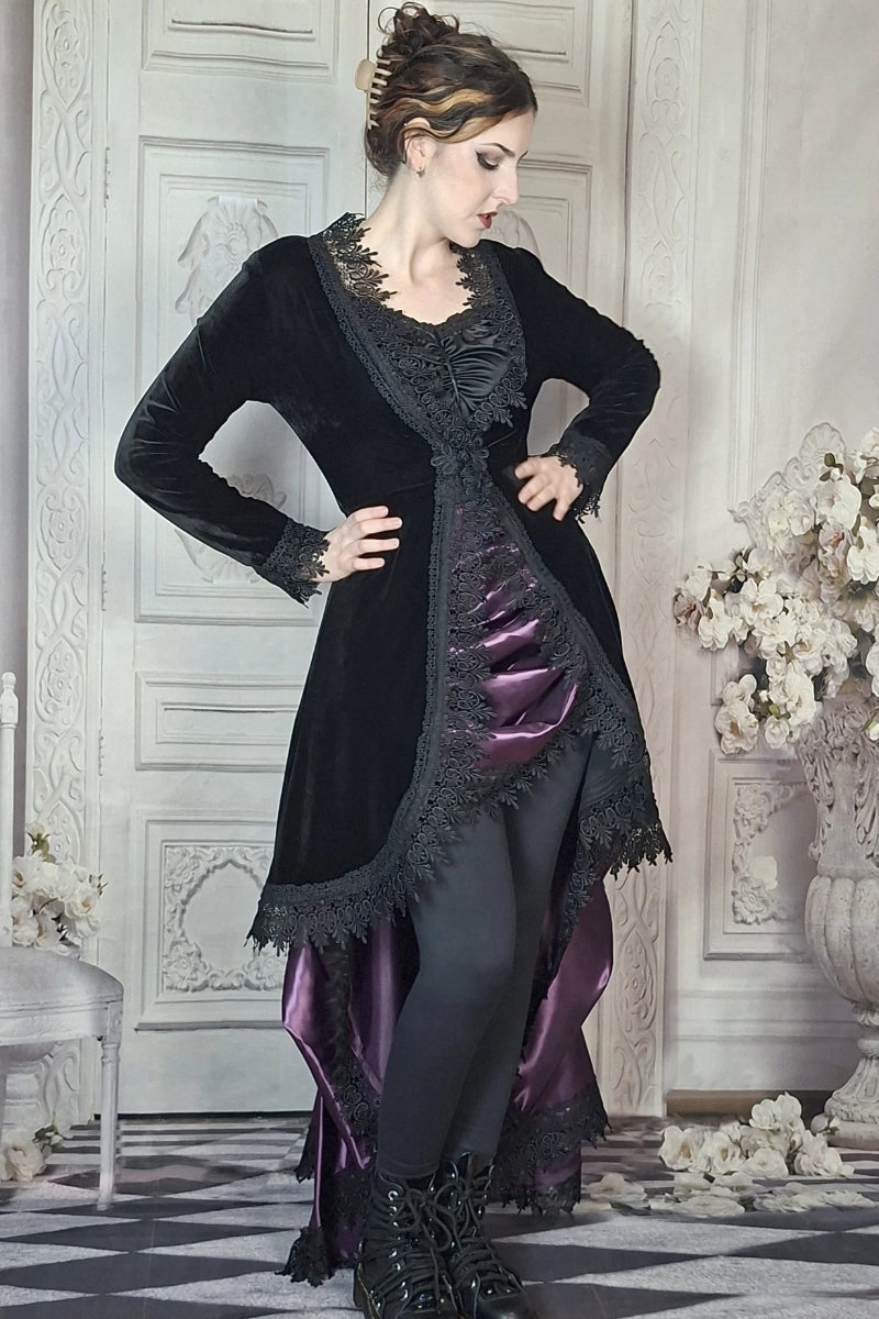 Woman in a black and purple Victorian-style dress standing in an elegant room with floral decorations.