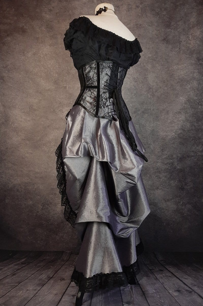 side back view showing the matching bustle skirt in the Australian made under bust tight lacing corset in a dark silver taffeta overlaid with delicate black lace and trimmed with black velvet ribbon down the corset bone channels