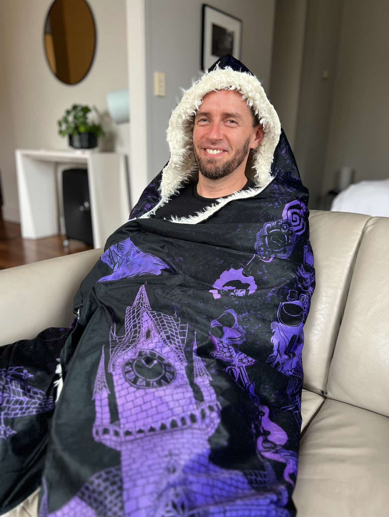 Steven Medway creator of Blood on the Clocktower wrapped up in his Grim Reader Wearable Blanket by Gallery Serpentine