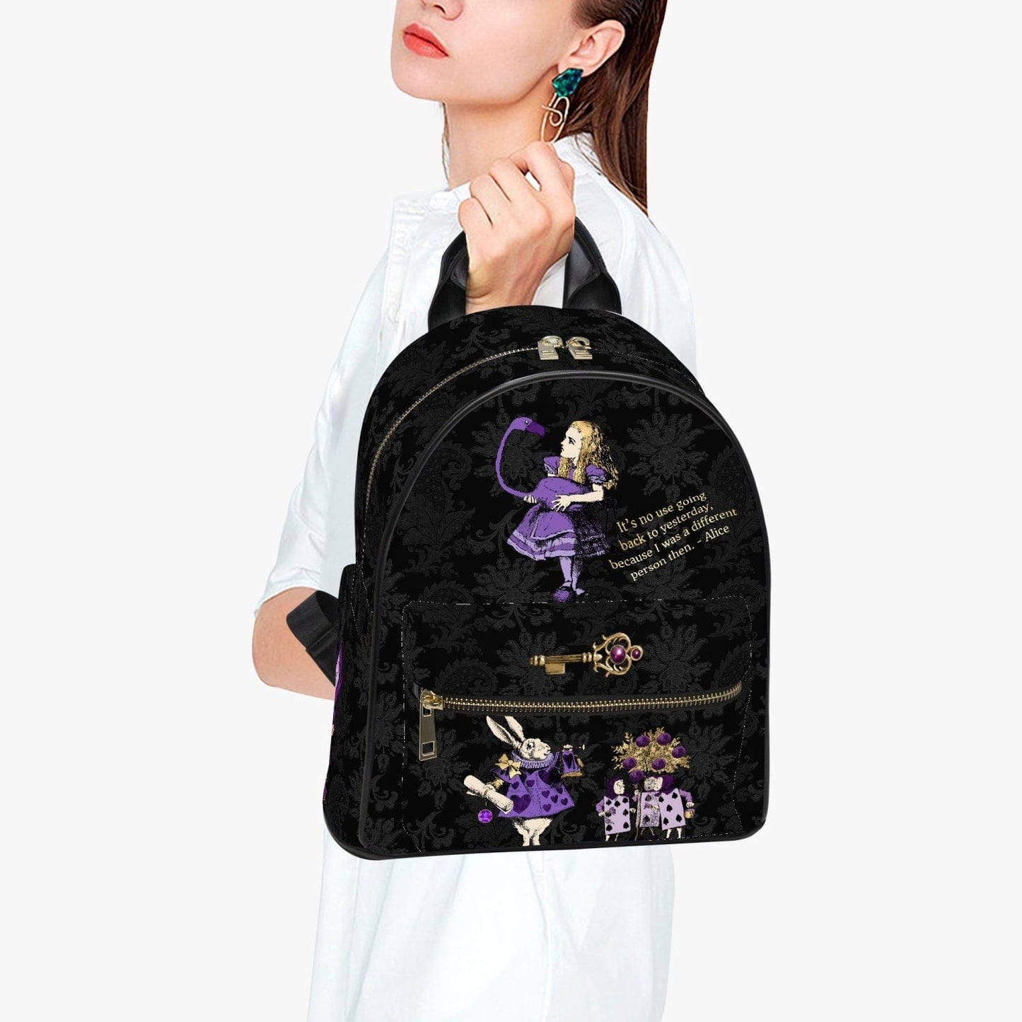 woman holding the black damask patterned mini backpack featuring Alice in Wonderland characters in purples and lilacs with a famous Alice quote