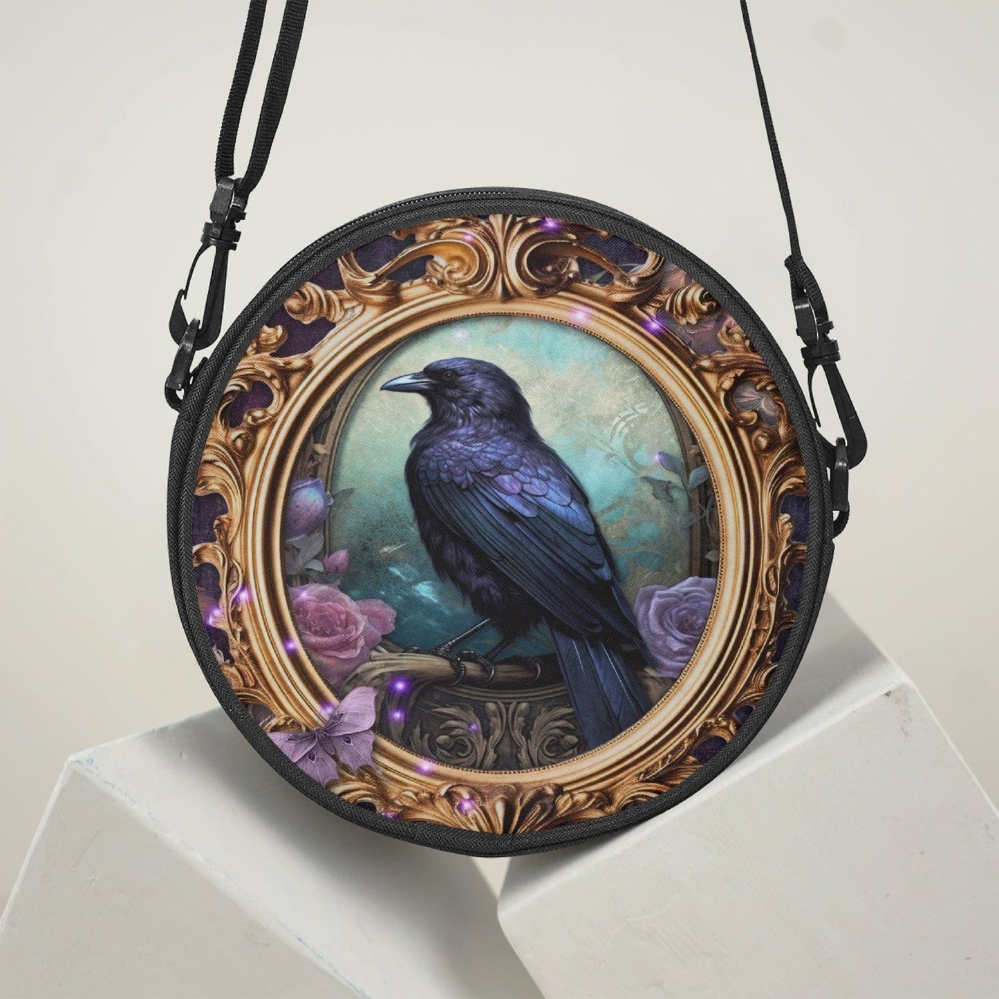 glossy black raven perched inside a gold rococo gilt frame features as the art work on this 23cm diameter round canvas cross body bag