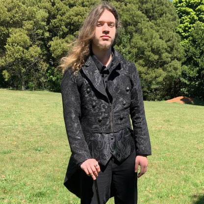 Man wearing a dark patterned coat standing in a grassy field with trees in the background