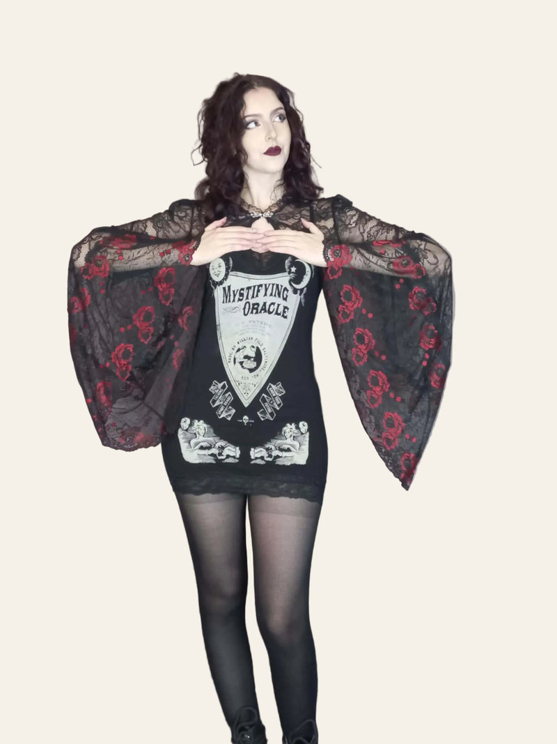 A model wearing a black gothic lace top with red embroidered roses and angel sleeves. The top features a filigree patterned metal clasp at the neck and is designed to sit open at the bust area.