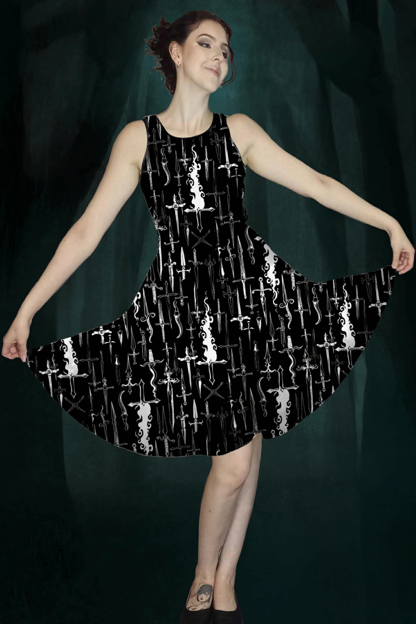 Woman wearing a black dress with white dagger & flames patterns against a dark green enchanted forest background