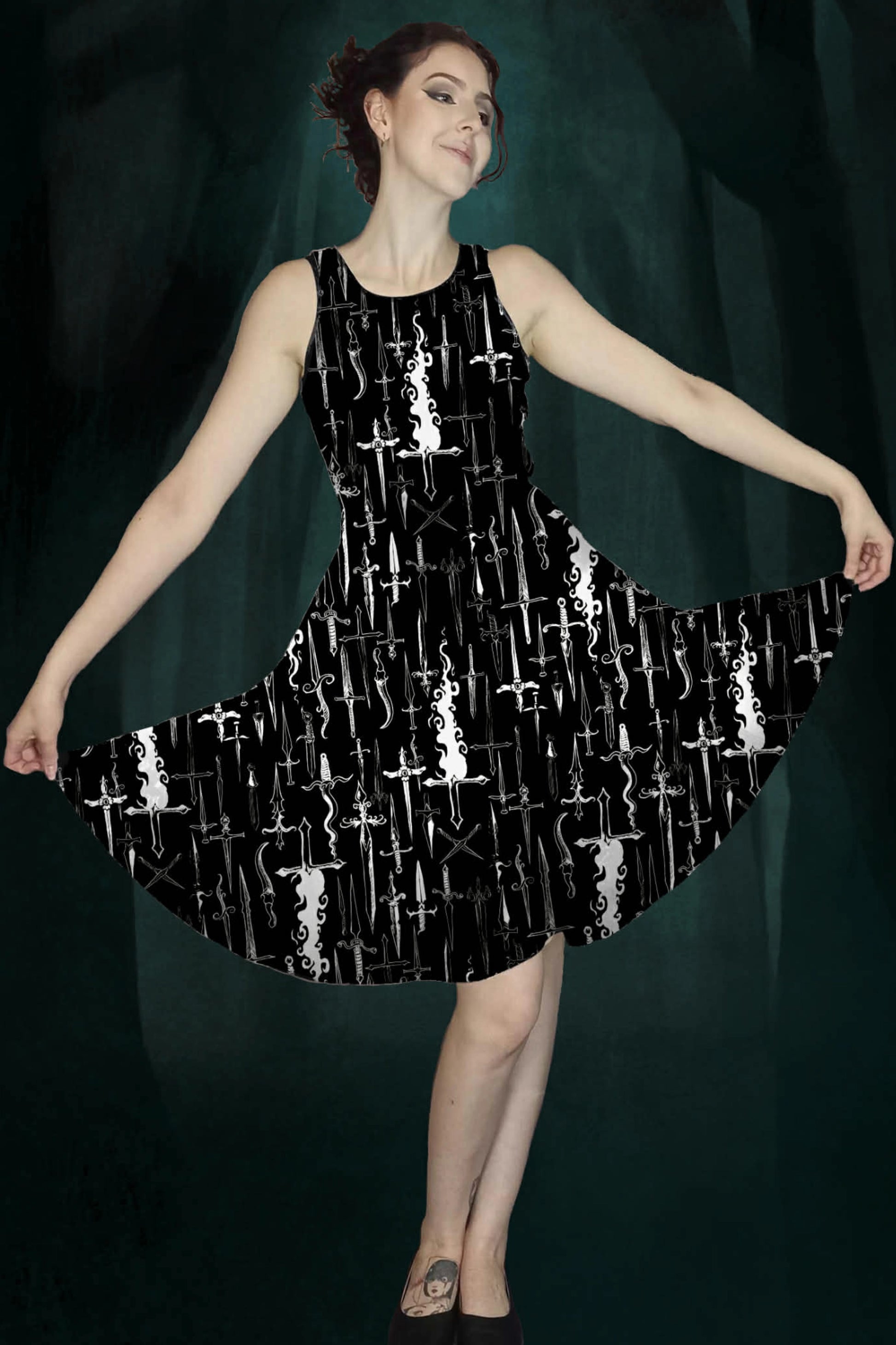 Woman wearing a black dress with white dagger & flames patterns against a dark green enchanted forest background