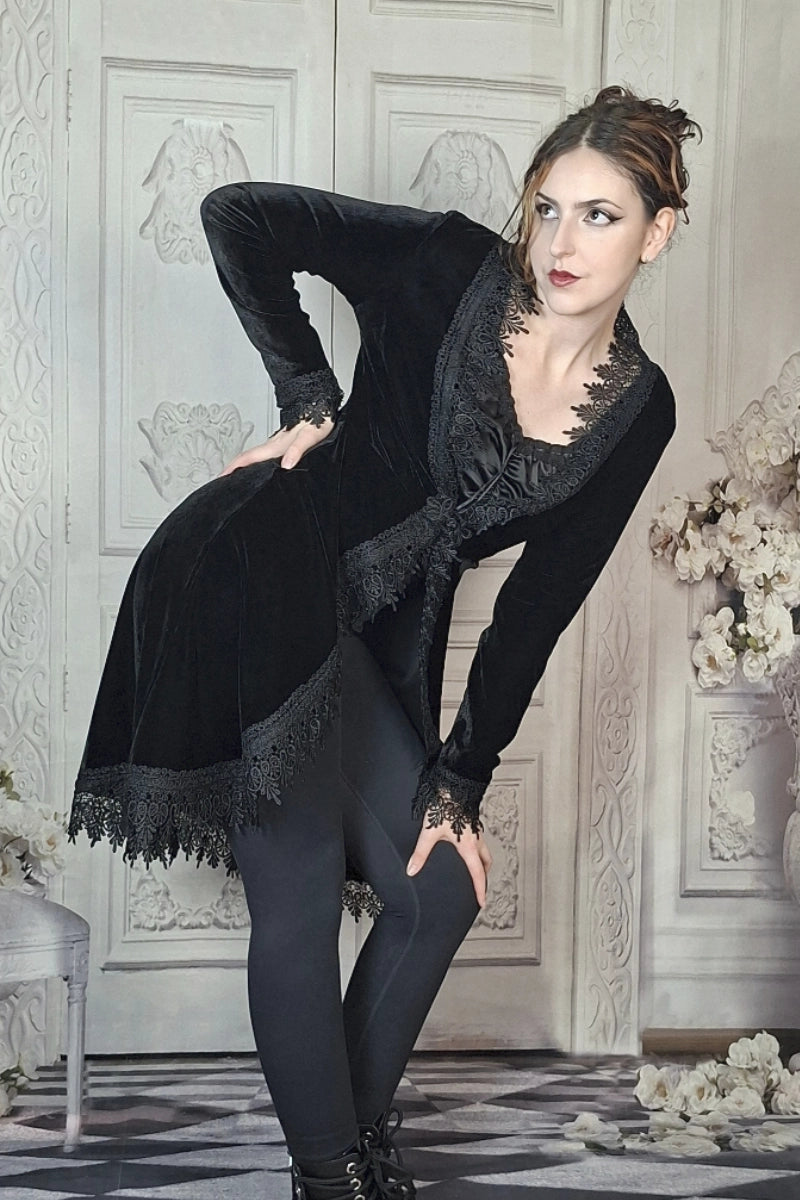 Woman in a black velvet outfit with lace details posing in an elegant room.