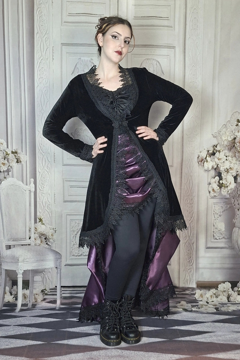 Woman in a black and purple Victorian-style dress standing in an elegant room with floral decorations.