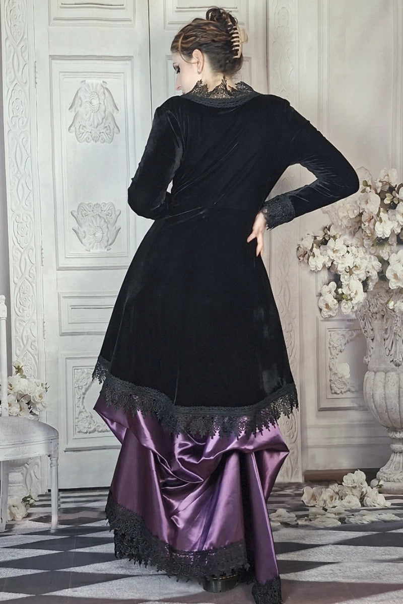 Woman wearing a black velvet and purple satin dress in an elegant interior setting.