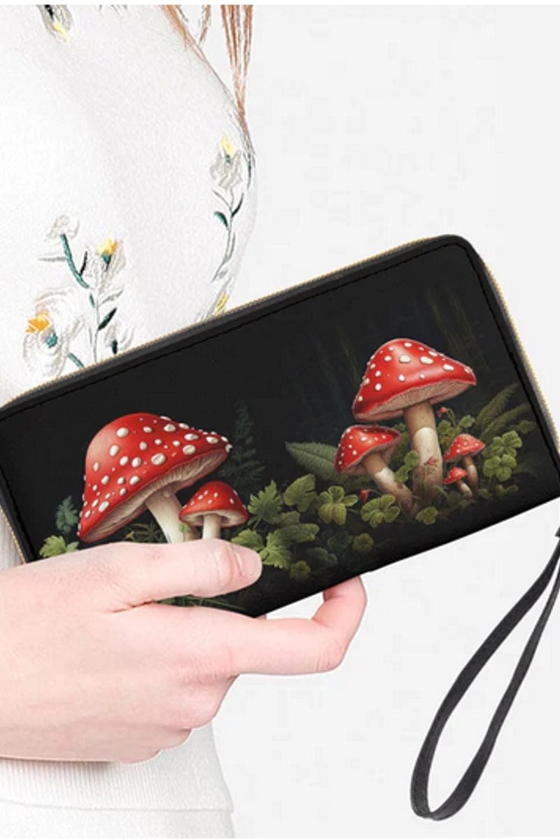 woman holding the red and white toadstools amongst green leaves on a cottagecore vegan wallet