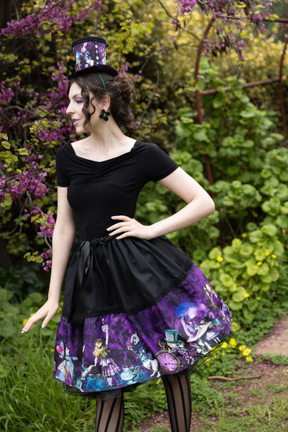 model wearing the Dark Alice mid length tea party skirt featuring all the Alice in Wonderland characters around the skirt on a purple and black damask print background