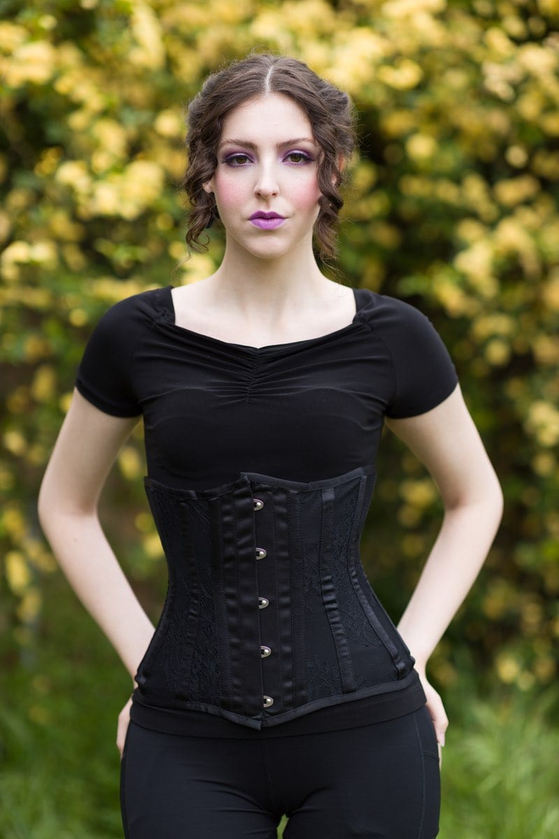 close up on lingerie model wearing Gallery Serpentine black lace corset with fajas shape wear