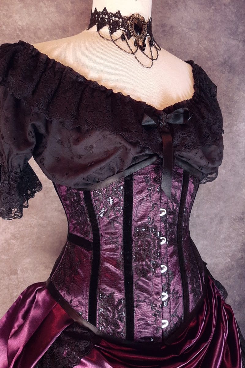 side front view of the amethyst satin with black lace overlay and black velvet ribbon on the bone channels on a mannequin torso with under bust top in black