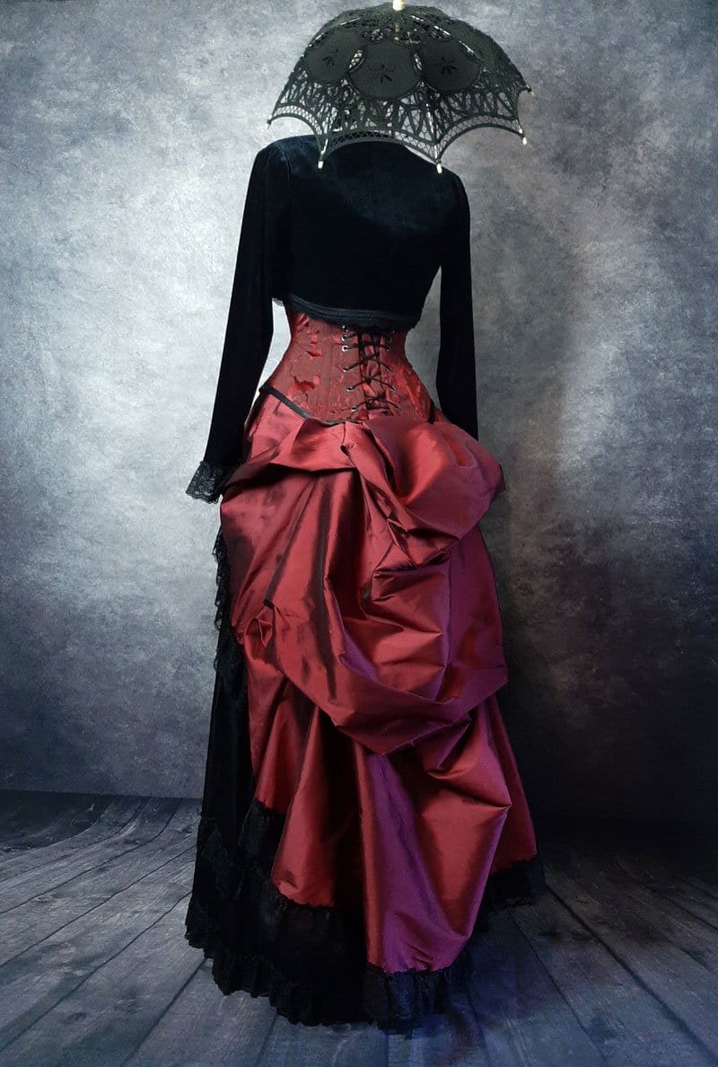 back view of the deluxe length victorian bustle skirt in garnet taffeta worn over a black satin under skirt and bustle cage