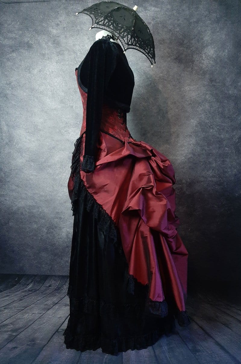 side view of the deluxe length victorian bustle skirt in garnet taffeta worn over a black satin under skirt and bustle cage