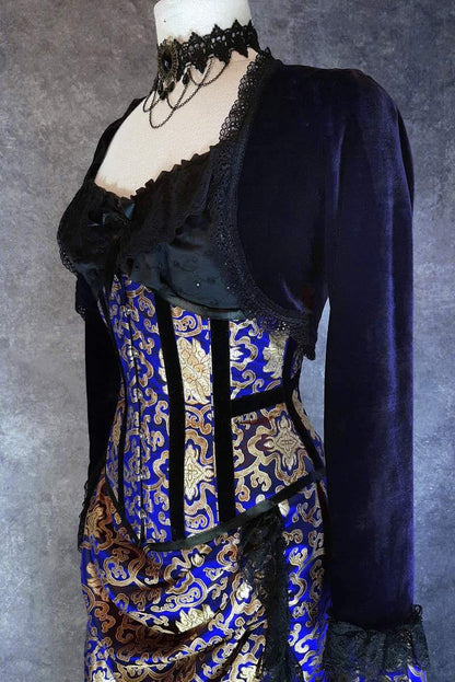 side front view showing waist compression of the royal blue and gold steel boned under bust corset worn on a mannequin with a black under corset top and dark purple velvet bolero shrug on top