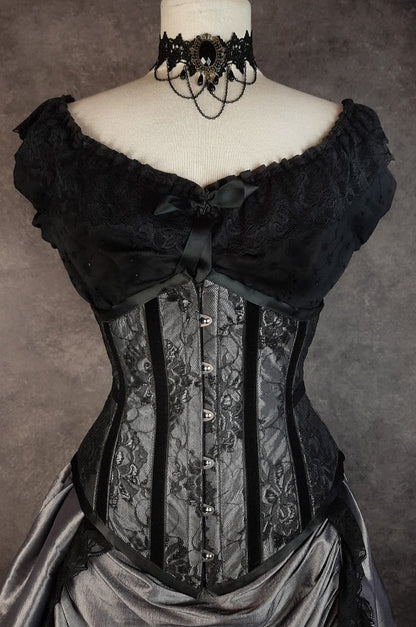 front view showing the waist compression in the Australian made under bust tight lacing corset in a dark silver taffeta overlaid with delicate black lace and trimmed with black velvet ribbon down the corset bone channels
