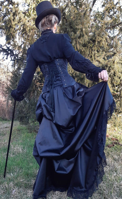 victorian woman shows the volume of fabric in the gothic victorian black sateen lace trimmed high low bustle skirt with adjustable waist sizing made in Australia for Gallery Serpentine