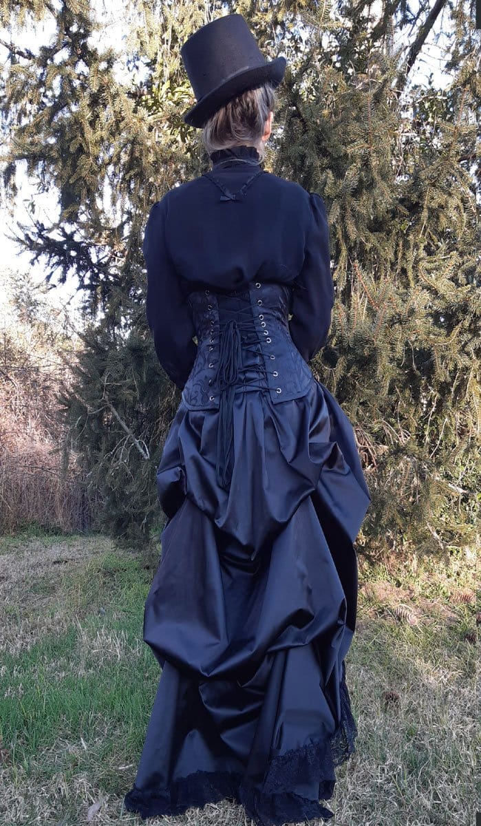 full back view showing black victorian blouse, steel boned corset and the gothic victorian black sateen lace trimmed high low bustle skirt with adjustable waist sizing made in Australia for Gallery Serpentine