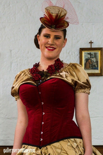 smiling plus size model in Gallery Serpentine blood red cotton velvet over bust corset at a fashion show